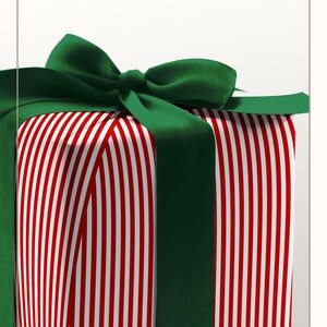 Puede incluir: Una caja de regalo cuadrada envuelta en papel con un patr&oacute;n de finas rayas verticales rojas y blancas. La caja est&aacute; atada con una cinta de sat&eacute;n verde oscuro ancha que forma un lazo en la parte superior. El texto ELEGANT RET STRIPE WRAPPING PAPER es visible.