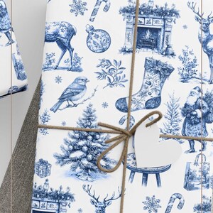Puede incluir: Papel de regalo blanco con un patr&oacute;n toile azul de motivos navide&ntilde;os que incluyen ciervos, calcetines, chimeneas, p&aacute;jaros, bastones de caramelo y adornos. El papel est&aacute; atado con cuerda marr&oacute;n y tiene una etiqueta blanca en forma de coraz&oacute;n.