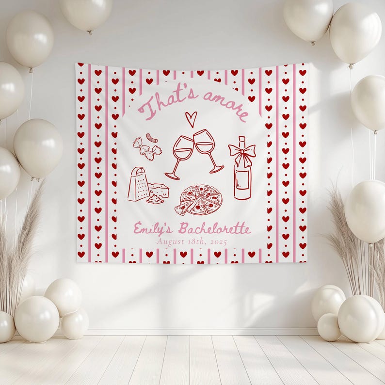 May include: A white backdrop with a red and pink banner that says "That's amore" with a heart and a wine glass clinking with another wine glass. There is a bottle of wine, a pizza, a grater, a piece of cheese, and a bow. The banner also says "Emily's Bachelorette August 18th, 2025".