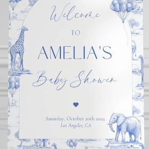 May include: A white welcome sign with blue text and illustrations of giraffes, elephants, and balloons. The sign reads "Welcome to Amelia's Baby Shower" and includes the date "Saturday, October 20th 2024" and location "Los Angeles, CA".
