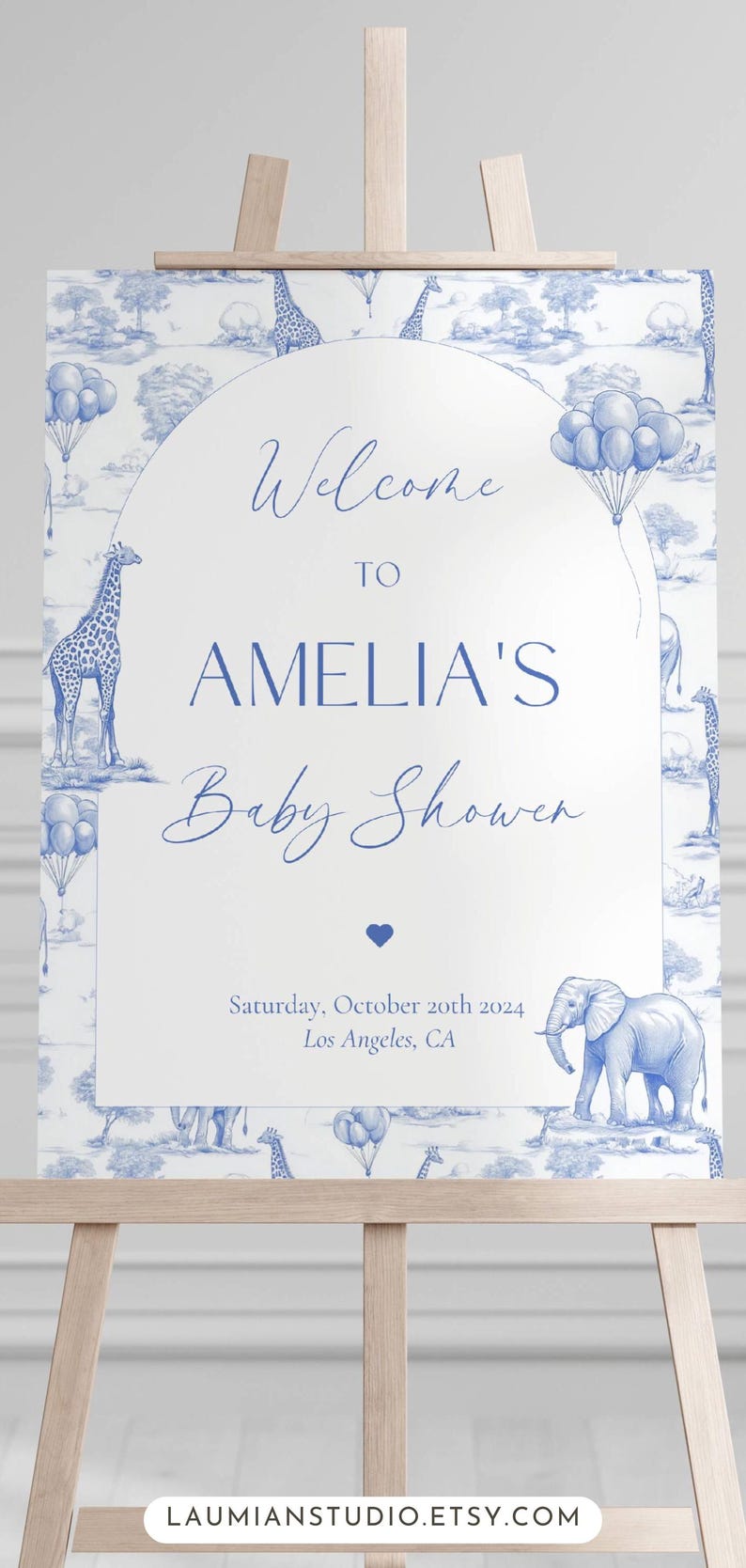 May include: A white welcome sign with blue text and illustrations of giraffes, elephants, and balloons. The sign reads "Welcome to Amelia's Baby Shower" and includes the date "Saturday, October 20th 2024" and location "Los Angeles, CA".