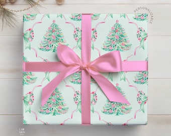 Puede incluir: Una caja de regalo cuadrada envuelta en papel verde menta claro con un patrón repetitivo de árboles de Navidad en acuarela, lazos rosas y cintas onduladas. Una cinta rosa ancha de acabado satinado está atada en un lazo alrededor del centro.