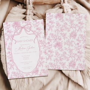 May include: Baby shower invitation with a pink floral design and text. The invitation features a bow and an oval frame with the words "Baby Shower" and event details. The back of the invitation has a pink floral pattern.