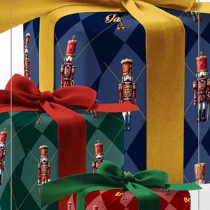 May include: Three gift boxes wrapped in nutcracker-patterned paper with argyle designs in blue, green, and red. The blue box has a gold ribbon, the green box has a red ribbon, and the red box has a green ribbon. Text reads NUTCRACKER WRAPPING PAPER.