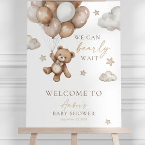 May include: A baby shower welcome sign on an easel. The sign features a teddy bear holding balloons, clouds, and stars. Text reads "We can bearly wait" and "Welcome to Amber's Baby Shower September 12, 2025."