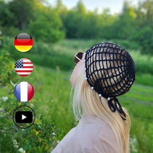 May include: A black crocheted hair net with a grid design, decorated with small white beads. The hair net is worn by a person with blonde hair, set against a blurred green backdrop of trees and grass.