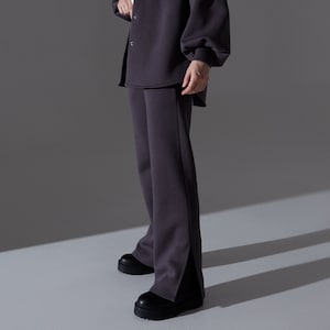 May include: A charcoal gray outfit consisting of a button-up shirt with a single chest pocket, matching wide-leg pants with side slits, and a bucket hat. The outfit is paired with black platform shoes. The model is wearing a white top underneath the shirt.