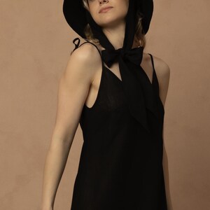 May include: A black sun hat with a wide brim and a matching black dress. The hat has a ribbon that ties under the chin. The dress is a simple, sleeveless design.
