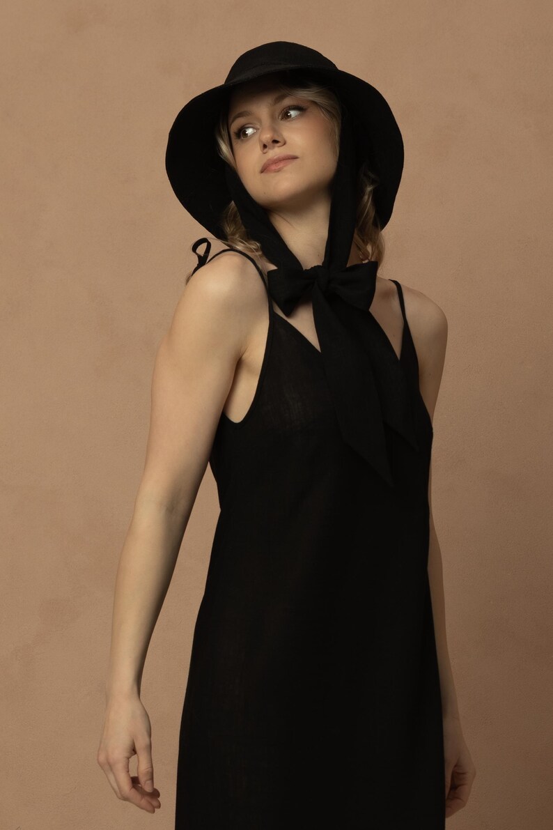 May include: A black sun hat with a wide brim and a matching black dress. The hat has a ribbon that ties under the chin. The dress is a simple, sleeveless design.
