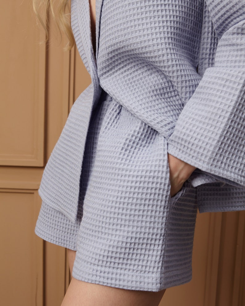 May include: A light blue waffle-weave robe and shorts set. The robe has wide sleeves and a tie belt. The shorts have pockets. The fabric has a textured, grid-like pattern. The set is made of a soft, comfortable material.