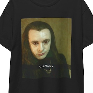 May include: Black t-shirt with a graphic print of a man with long dark hair and a gold chain. The text "U up? haha x" is printed below the image.