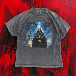May include: A grey t-shirt with a graphic of a crowned king holding orbs of light, and the text "you are acting crazy first of all I'm not acting". The shirt has a vintage, washed appearance.