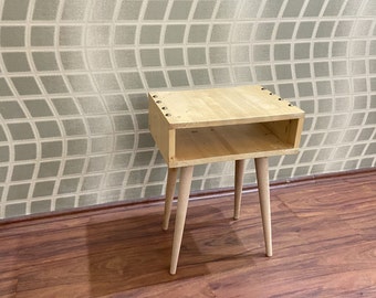 May include: A small wooden end table with a shelf and four legs. The table is made of light wood and has a natural finish. The table has a simple design and is perfect for a bedroom or living room.