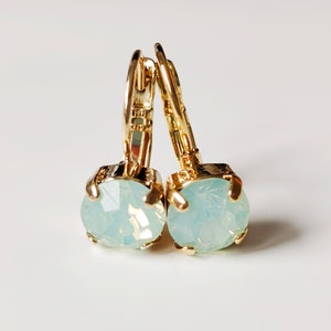 May include: A pair of gold hoop earrings with a light blue opal stone on each earring.