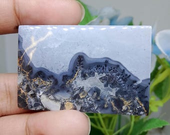 Puede incluir: Una piedra preciosa rectangular con un patrón de paisaje. La piedra presenta un fondo azul claro con vetas azul oscuro, negras y doradas. El diseño se asemeja a una cordillera o una escena natural.