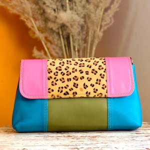 Könnte beinhalten: Eine farbenfrohe Clutch mit einem Leopardenmuster-Mittelteil. Die Tasche hat eine Kombination aus rosa, blauem und grünem Leder. Die Clutch ist rechteckig und scheint aus hochwertigen Materialien gefertigt zu sein.