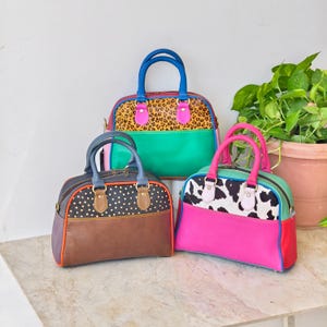 May include: Three structured handbags with dual top handles. The back bag features a leopard print top and green base. The front left bag has a brown base with a black and gold polka dot top. The front right bag has a pink base and cow print top.