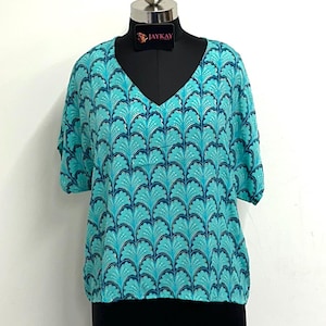 May include: A turquoise blue and gold patterned short-sleeved top with a V-neck. The top has a relaxed fit and is made of a lightweight fabric. The label "JAYKAY" is visible on the top.