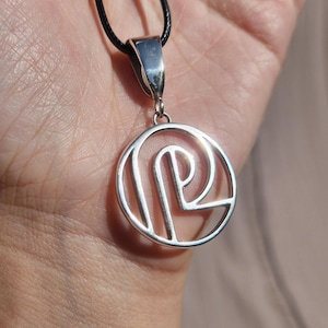 May include: A silver necklace with a circular pendant featuring a stylized letter P. The pendant is attached to a black cord.