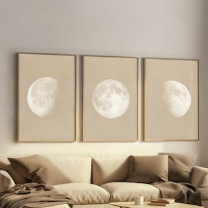 Peut inclure: Trois impressions encadrées représentant les phases de la lune. Chaque impression présente une étape différente du cycle lunaire sur un fond beige. Les cadres sont de couleur marron clair. Les impressions sont au-dessus d'un canapé sectionnel crème avec des coussins bruns et une couverture brune.