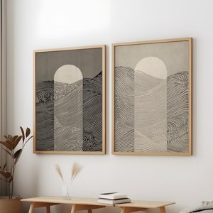 Pode incluir: Duas impressões de arte abstrata emolduradas. Cada impressão apresenta uma paisagem estilizada com uma forma de sol ou lua e linhas onduladas em tons de cinza e bege. As molduras são de madeira clara. A obra de arte está pendurada acima de um banco de madeira.