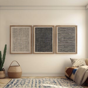 May include: Three framed abstract art prints. The prints feature black and white geometric patterns: a grid, a series of squares, and horizontal lines. The frames are a light brown color, and the art is displayed on a white wall.