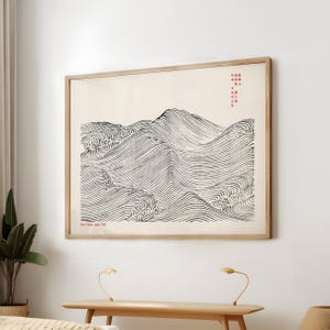 May include: A framed print of a Japanese landscape. The artwork features black and white wavy lines depicting mountains and valleys. The print has Japanese text in red and is set in a light wood frame.