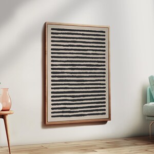 May include: A framed abstract art piece featuring a beige background with evenly spaced, horizontal black lines. The artwork is encased in a light-colored wooden frame, creating a minimalist aesthetic. The piece is mounted on a white wall.