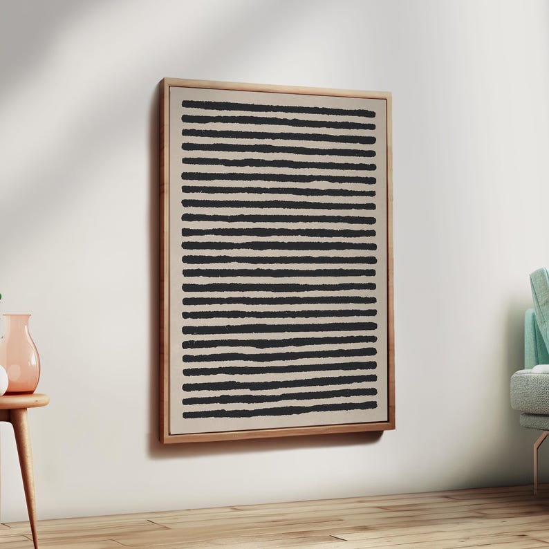 May include: A framed abstract art piece featuring a beige background with evenly spaced, horizontal black lines. The artwork is encased in a light-colored wooden frame, creating a minimalist aesthetic. The piece is mounted on a white wall.