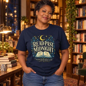 Può includere: Una t-shirt blu navy a maniche corte con una stampa grafica di un libro aperto, una mezzaluna e stelle con il testo "READ PAST MIDNIGHT" e "AFTER HOURS BOOK CLUB" in un carattere decorativo, circondato da viticci floreali blu e gialli.