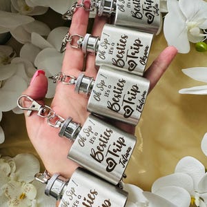 May include: Five silver hip flasks with engraved text that reads "Oh Sip! It's a Besties Trip" with a heart and each flask has a different name engraved below the text. The names are Julia, Oksana, Tatiana, Alessinea.