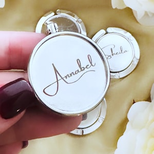May include: Silver-toned, round, foldable handbag hook with the name "Annabel" engraved in cursive script.