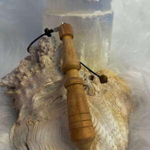 May include: A wooden pendulum with a brown cord and a silver bead. The pendulum is resting on a white and brown seashell.