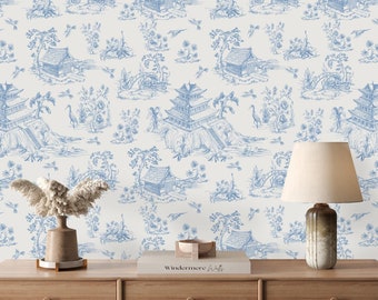 May include: Blue and white toile wallpaper with a repeating pattern of pagodas, bridges, and flowers. The wallpaper is displayed on a wooden dresser with a lamp and a book on top.