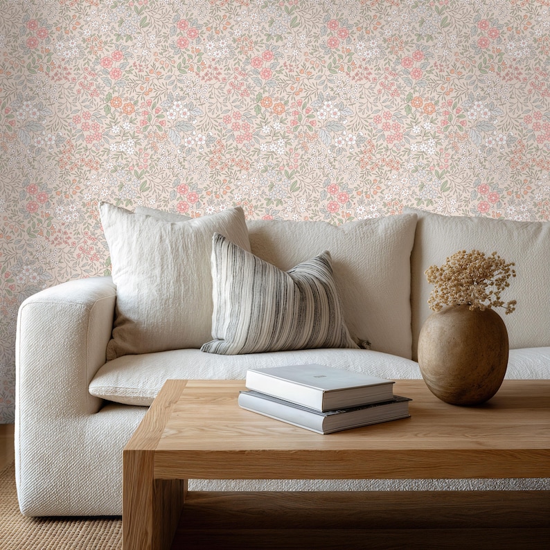 This image showcases the wallpaper pattern in a living room setting. The pattern features a ditsy floral blossom design. The flowers are illustrated in shades of peach, coral, pink, and white against a beige background.
