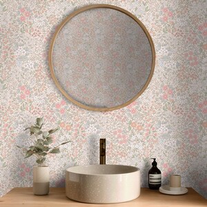 This image showcases the wallpaper pattern in a bathroom setting. The pattern features a ditsy floral blossom design. The flowers are illustrated in shades of peach, coral, pink, and white against a beige background.