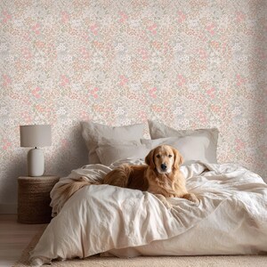 This image showcases the wallpaper pattern in a bedroom setting. The pattern features a ditsy floral blossom design. The flowers are illustrated in shades of peach, coral, pink, and white against a beige background.