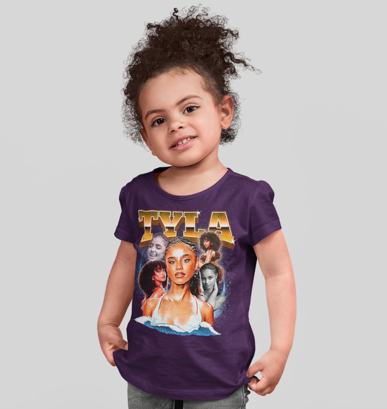 May include: A purple short-sleeved t-shirt with a vintage-style graphic of a woman's face with the text "TYLA" in gold letters.