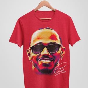 May include: Red t-shirt with a colorful illustration of a man wearing sunglasses and a signature.