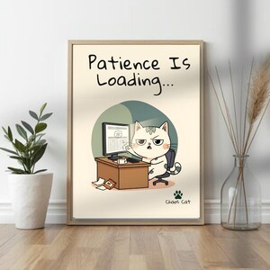 May include: A framed print featuring a cartoon cat at a desk with a computer. The text "Patience Is Loading..." is at the top. The cat has an annoyed expression. The print is in a light-colored wooden frame.