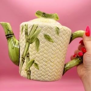 May include: A white ceramic teapot with a woven pattern and green bamboo accents. The teapot has a lid and a handle.