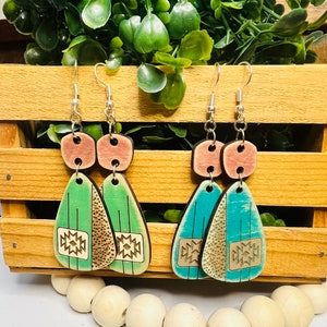 May include: A pair of wooden earrings with a geometric pattern. The earrings are teal, green, and brown with a pink accent.