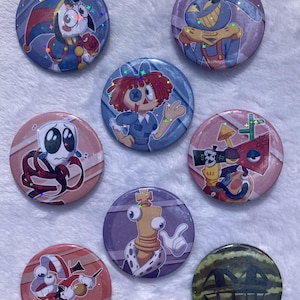 May include: Nine circular pin badges with cartoon illustrations. The badges showcase diverse characters in bright colours, including a jester, a scarecrow, a doll, and a watermelon with a face.