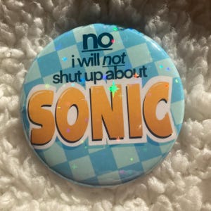 Op de afbeelding: Een blauw-wit geblokte knop met de tekst "no i will not shut up about SONIC" in gele letters.