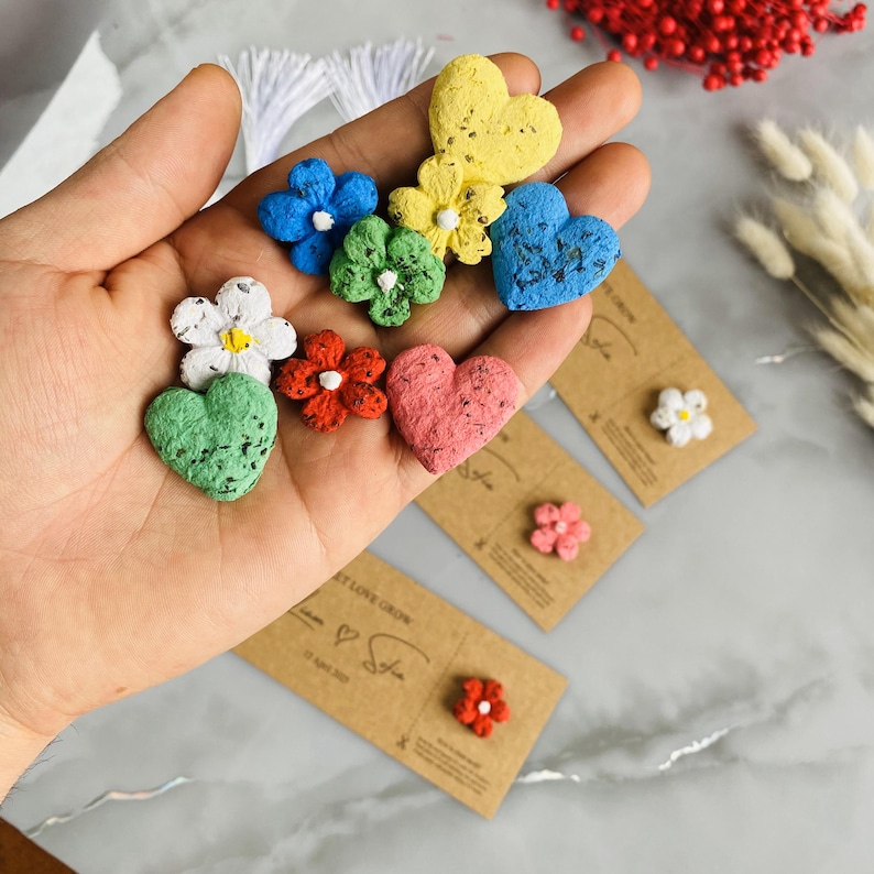 May include: A collection of colorful seed paper shapes, including flowers and hearts, in shades of blue, green, yellow, red, and pink. Small cards with flower-shaped seeds are also visible. The items are likely for planting.