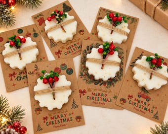 May include: Five white scalloped wax melts attached to brown kraft paper cards. Each card features Christmas-themed illustrations and the text Merry Christmas From Emily. The wax melts are decorated with twine and small red berries.