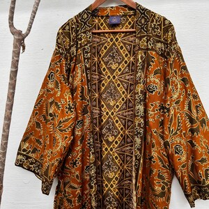 Puede incluir: Un kimono de seda marrón y dorado con un patrón geométrico. El kimono tiene una silueta larga y fluida y es perfecto para superponer sobre un vestido o pantalones.