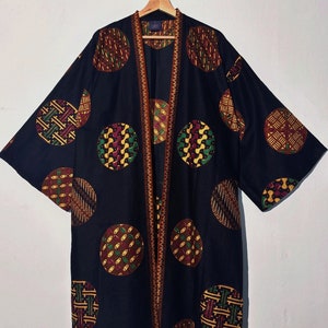 Puede incluir: Un kimono negro con un patrón geométrico colorido de círculos. El kimono tiene un ribete marrón y está colgado en una percha de madera.