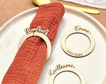 May include: Three wooden napkin rings with personalized names and dates. The rings are light brown and have a simple, elegant design. The names are "Raphael", "Emma", and "Guillaume". The dates are "19.07.2025".