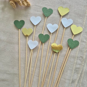 Peut inclure: Une collection de décorations en forme de cœur sur des brochettes en bois. Les décorations sont de différentes couleurs, dont vert pailleté, blanc et or. Ces décorations sont idéales pour les gâteaux, les cupcakes ou autres friandises festives.